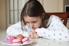 Ragazza sveglia che esamina tristemente i maccheroni e zefir fotografia stock Ragazza sveglia che esamina tristemente i maccheroni e zefir fotografia stock