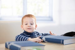Ragazzino bello che si siede alla tabella con i libri fotografie stock Ragazzino bello che si siede alla tabella con i libri fotografie stock