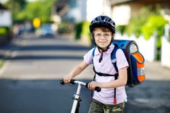 Ragazzo attivo del bambino della scuola nella guida del casco di sicurezza con il suo motorino nella città con lo zaino il giorno immagini stock Ragazzo attivo del bambino della scuola nella guida del casco di sicurezza con il suo motorino nella città con lo zaino il giorno immagini stock