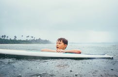 Ragazzo che impara praticare il surfing sotto la pioggia tropicale E immagine stock Ragazzo che impara praticare il surfing sotto la pioggia tropicale E immagine stock
