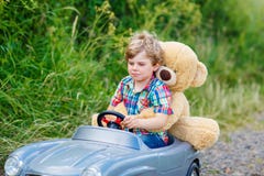 Ragazzo del bambino che conduce la grande automobile del giocattolo con un orso, all'aperto Fotografia Stock Libera da Diritti Ragazzo del bambino che conduce la grande automobile del giocattolo con un orso, all'aperto Fotografia Stock Libera da Diritti