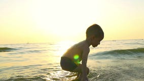 Ragazzo del bambino che gioca con acqua sul mare, nelle onde ricevute, contro lo sfondo del tramonto stock footage Ragazzo del bambino che gioca con acqua sul mare, nelle onde ricevute, contro lo sfondo del tramonto stock footage