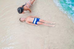Ragazzo e ragazza svegli divertendosi sulla spiaggia tropicale soleggiata Trovandosi sulla sabbia, onde meravigliose intorno loro Immagini Stock Ragazzo e ragazza svegli divertendosi sulla spiaggia tropicale soleggiata Trovandosi sulla sabbia, onde meravigliose intorno loro Immagini Stock