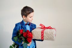 Ragazzo sorridente con il mazzo dei fiori e di un regalo su un fondo leggero immagine stock Ragazzo sorridente con il mazzo dei fiori e di un regalo su un fondo leggero immagine stock