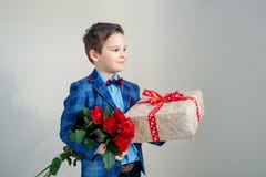 Ragazzo sorridente con il mazzo dei fiori e di un regalo su un fondo leggero fotografia stock libera da diritti Ragazzo sorridente con il mazzo dei fiori e di un regalo su un fondo leggero fotografia stock libera da diritti