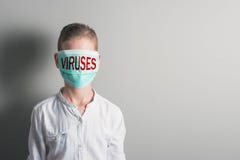 Ragazzo in una maschera medica con i VIRUS rossi dell'iscrizione sul suo fronte su fondo luminoso fotografia stock libera da diritti Ragazzo in una maschera medica con i VIRUS rossi dell'iscrizione sul suo fronte su fondo luminoso fotografia stock libera da diritti