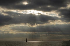 Raios de sol que quebram através da nebulosidade, uma navigação do veleiro em um lago perto de Amsterdão fotografia de stock Raios de sol que quebram através da nebulosidade, uma navigação do veleiro em um lago perto de Amsterdão fotografia de stock