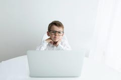 Rapaz pequeno bonito que usa o port?til ao fazer trabalhos de casa contra o fundo branco fotos de stock Rapaz pequeno bonito que usa o port?til ao fazer trabalhos de casa contra o fundo branco fotos de stock