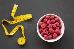 Raw raspberries in a pink bowl with measuring tape on black surface, top view. Healthy eating and dieting. From above, overhead stock image Raw raspberries in a pink bowl with measuring tape on black surface, top view. Healthy eating and dieting. From above, overhead stock image