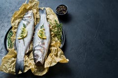 Raw sea bass with rosemary, thyme and lemon. Black background, top view, space for text. stock image Raw sea bass with rosemary, thyme and lemon. Black background, top view, space for text. stock image