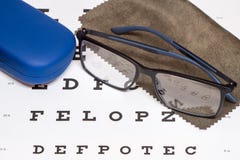 Reading black eyeglasses, brown microfiber cleaning cloth and blue protective case on white eye chart royalty free stock images Reading black eyeglasses, brown microfiber cleaning cloth and blue protective case on white eye chart royalty free stock images