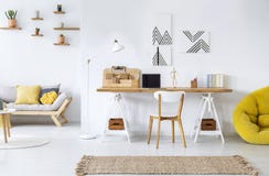 Modern home office interior with graphics, desk, sofa and yellow pouf