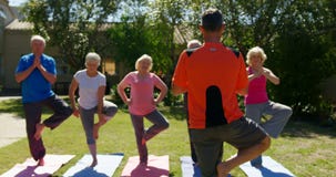Rear view of Caucasian male trainer training senior people in performing yoga at the garden of n 4k stock footage Rear view of Caucasian male trainer training senior people in performing yoga at the garden of n 4k stock footage