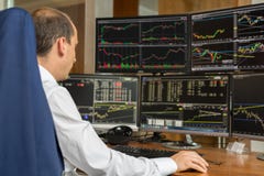 Rear view of stock trader analyzing data at multiple computer screens.