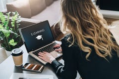 Rear view. Young woman is working on laptop with inscription on screen e-learning and image of square academic cap. royalty free stock photography Rear view. Young woman is working on laptop with inscription on screen e-learning and image of square academic cap. royalty free stock photography
