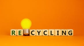 Recycling concept. Wooden cubes with word `Recycling`. Yellow light bulb. Beautiful orange background. Business, ecological and