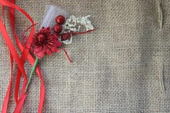 Red artificial flower with red festive ribbons on a background of brown old linen fabric texture, linen natural material with a co. Arse perpendicular Royalty Free Stock Image Red artificial flower with red festive ribbons on a background of brown old linen fabric texture, linen natural material with a co. Arse perpendicular Royalty Free Stock Image