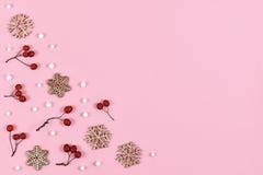Red berries, white snowballs and wooden snowflake Christmas ornaments in corners of light pink background with copy space