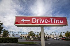 Red rectangular sign reading Drive Thru for fast food retaurant against blue sky and clouds