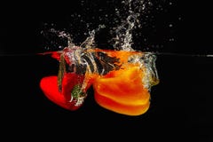 Red and yellow bellpepper falling into the water. With a splash on a black background Royalty Free Stock Image Red and yellow bellpepper falling into the water. With a splash on a black background Royalty Free Stock Image