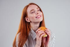 Redheared hungry woman in striped shirt eating USA burger visa traveler white background studio