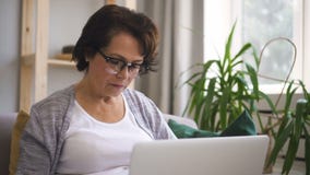 Reife Frau mit dem braunen Haar, in den Gläsern sitzt am Sofa stock footage Reife Frau mit dem braunen Haar, in den Gläsern sitzt am Sofa stock footage