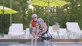 Reife Paare des Porträts, die wenig Enkelin am Rand des Pools umarmen Großmutter, Großvater und Enkelkind stock video Reife Paare des Porträts, die wenig Enkelin am Rand des Pools umarmen Großmutter, Großvater und Enkelkind stock video