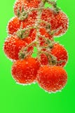 Reife rote Kirschtomaten auf der Niederlassung versenkt in Wasser mit Blasen lizenzfreies stockfoto Reife rote Kirschtomaten auf der Niederlassung versenkt in Wasser mit Blasen lizenzfreies stockfoto