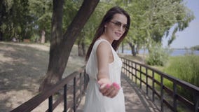 Reizende brunette tragende Sonnenbrille des jungen Mädchens des Porträts und langes weißes Sommermodekleid, die entlang eine Holz stock video footage Reizende brunette tragende Sonnenbrille des jungen Mädchens des Porträts und langes weißes Sommermodekleid, die entlang eine Holz stock video footage