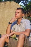 Relaxed attractive smiling man sit in a shirt, shorts and hours near large stone Stock Images Relaxed attractive smiling man sit in a shirt, shorts and hours near large stone Stock Images