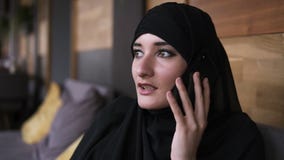 Respondendo ao telefonema Mulher muçulmana bonita nova com composição no hijab que fala no telefone e no sorriso, sentando-se no video estoque Respondendo ao telefonema Mulher muçulmana bonita nova com composição no hijab que fala no telefone e no sorriso, sentando-se no video estoque