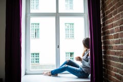 Resting and thinking woman. Calm girl with cup of tea or coffee sitting and drinking on the window-sill at home. royalty free stock photos Resting and thinking woman. Calm girl with cup of tea or coffee sitting and drinking on the window-sill at home. royalty free stock photos