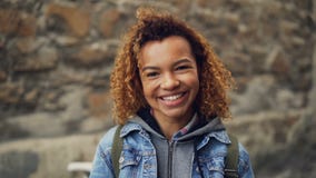 Retrato cercano de la cámara lenta de reír a la muchacha afroamericana con el pelo rizado ligero en la chaqueta del dril de algod almacen de metraje de vídeo Retrato cercano de la cámara lenta de reír a la muchacha afroamericana con el pelo rizado ligero en la chaqueta del dril de algod almacen de metraje de vídeo
