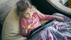 Retrato da menina bonita, uma criança que se encontre no sofá sob a cobertura e em jogos no tablet pc filme Retrato da menina bonita, uma criança que se encontre no sofá sob a cobertura e em jogos no tablet pc filme