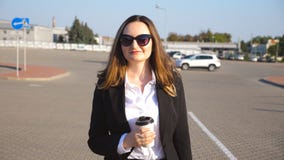 Retrato da mulher de negócios nova com xícara de café que anda perto do auto estacionamento no dia ensolarado Mulher de negócio f filme Retrato da mulher de negócios nova com xícara de café que anda perto do auto estacionamento no dia ensolarado Mulher de negócio f filme