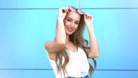 Retrato da mulher de sorriso da forma da beleza com penteado do voo, em óculos de sol de néon cor-de-rosa no fundo azul ocasional filme Retrato da mulher de sorriso da forma da beleza com penteado do voo, em óculos de sol de néon cor-de-rosa no fundo azul ocasional filme
