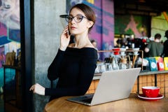 Retrato da mulher nova bonita do freelancer na cafetaria Senhora bonita com o telefone esperto em suas mãos usando o portátil e o imagem de stock royalty free Retrato da mulher nova bonita do freelancer na cafetaria Senhora bonita com o telefone esperto em suas mãos usando o portátil e o imagem de stock royalty free