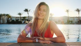 Retrato de la chica joven sonriente, mirando la c?mara Mujer hermosa en el traje de ba?o rojo que se sienta en la piscina azul en metrajes Retrato de la chica joven sonriente, mirando la c?mara Mujer hermosa en el traje de ba?o rojo que se sienta en la piscina azul en metrajes