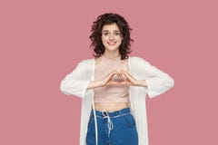 Retrato de la mujer joven morena hermosa con el peinado rizado en el estilo sport que se coloca con gesto de mano del amor y que fotografía de archivo Retrato de la mujer joven morena hermosa con el peinado rizado en el estilo sport que se coloca con gesto de mano del amor y que fotografía de archivo