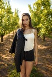 Retrato de la situación morena de la belleza en el paisaje verde de la huerta de fruta, ella guarda la chaqueta de cuero en el br imágenes de archivo libres de regalías Retrato de la situación morena de la belleza en el paisaje verde de la huerta de fruta, ella guarda la chaqueta de cuero en el br imágenes de archivo libres de regalías