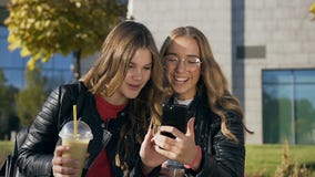 Retrato de los dos mejores amigos elegantes de los estudiantes que beben el jugo fresco, leyendo algo en el smartphone y metrajes Retrato de los dos mejores amigos elegantes de los estudiantes que beben el jugo fresco, leyendo algo en el smartphone y metrajes