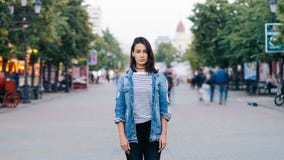 Retrato de time lapse del estudiante de mujer cansado que se coloca solamente en centro de ciudad y que mira la cámara con la car almacen de metraje de vídeo Retrato de time lapse del estudiante de mujer cansado que se coloca solamente en centro de ciudad y que mira la cámara con la car almacen de metraje de vídeo