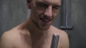 Retrato de um homem que canta emocionalmente no chuveiro usando a cabeça de chuveiro com água de fluxo em vez de um microfone filme Retrato de um homem que canta emocionalmente no chuveiro usando a cabeça de chuveiro com água de fluxo em vez de um microfone filme