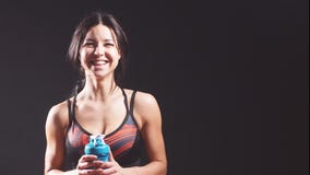 Retrato de una muchacha alegre atlética en el estudio en un fondo negro con una botella de agua almacen de video Retrato de una muchacha alegre atlética en el estudio en un fondo negro con una botella de agua almacen de video