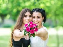 Retrato Defocused de duas jovens mulheres bonitas que mantêm unido o ramalhete do casamento e que olham na câmera no parque verde imagens de stock Retrato Defocused de duas jovens mulheres bonitas que mantêm unido o ramalhete do casamento e que olham na câmera no parque verde imagens de stock