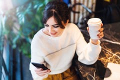 Retrato del caf? que se sienta de la muchacha, usando smartphone La mujer joven lee el mensaje de texto en el tel?fono mientras q foto de archivo Retrato del caf? que se sienta de la muchacha, usando smartphone La mujer joven lee el mensaje de texto en el tel?fono mientras q foto de archivo