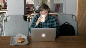 Retrato del hombre de negocios joven ocupado que se sienta con el vidrio de la bebida y la hamburguesa en interior del restaurant almacen de video Retrato del hombre de negocios joven ocupado que se sienta con el vidrio de la bebida y la hamburguesa en interior del restaurant almacen de video