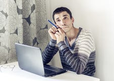 Retrato del hombre joven en ropa de sport en el funcionamiento del trabajo en el ordenador port?til que mira con la cara pensativ imagen de archivo libre de regalías Retrato del hombre joven en ropa de sport en el funcionamiento del trabajo en el ordenador port?til que mira con la cara pensativ imagen de archivo libre de regalías