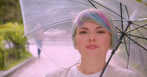 Retrato del primer de la hembra caucásica linda joven con el pelo teñido que sostiene un paraguas que mira la cámara que fija su almacen de metraje de vídeo Retrato del primer de la hembra caucásica linda joven con el pelo teñido que sostiene un paraguas que mira la cámara que fija su almacen de metraje de vídeo