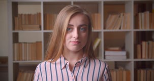 Retrato del primer del estudiante caucásico bonito joven que mira la cámara que sonríe con timidez en la biblioteca de universida almacen de metraje de vídeo Retrato del primer del estudiante caucásico bonito joven que mira la cámara que sonríe con timidez en la biblioteca de universida almacen de metraje de vídeo